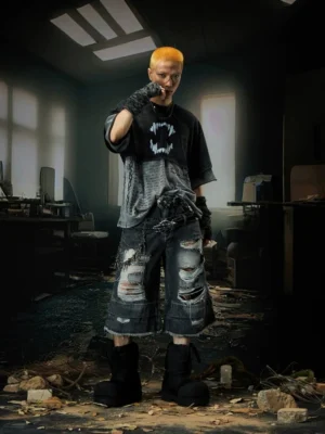 Male model with yellow buzzcut wearing a washed black layered punk graphic T-shirt with distressed denim shorts and streetwear accessories