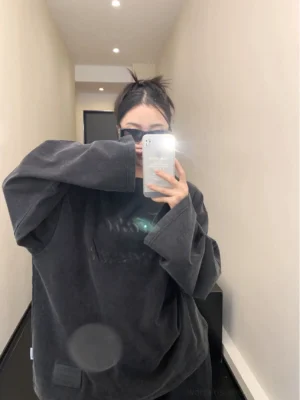Front mirror view of a washed black oversized fleece crewneck sweatshirt with tonal cursive script print, dropped shoulders, and long relaxed sleeves