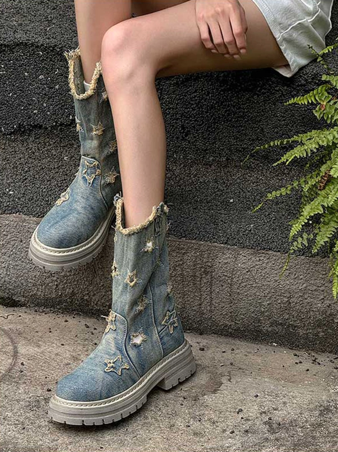 Three-quarter outdoor view of washed blue denim platform boots with star embroidery, frayed edges, and rugged lug outsole