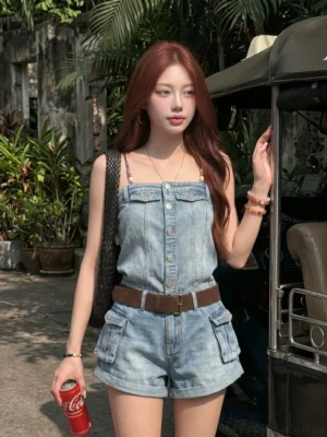 Three-quarter view of a vintage washed denim camisole romper featuring beaded straps, chest flap pockets, side cargo pockets, and utility streetwear styling