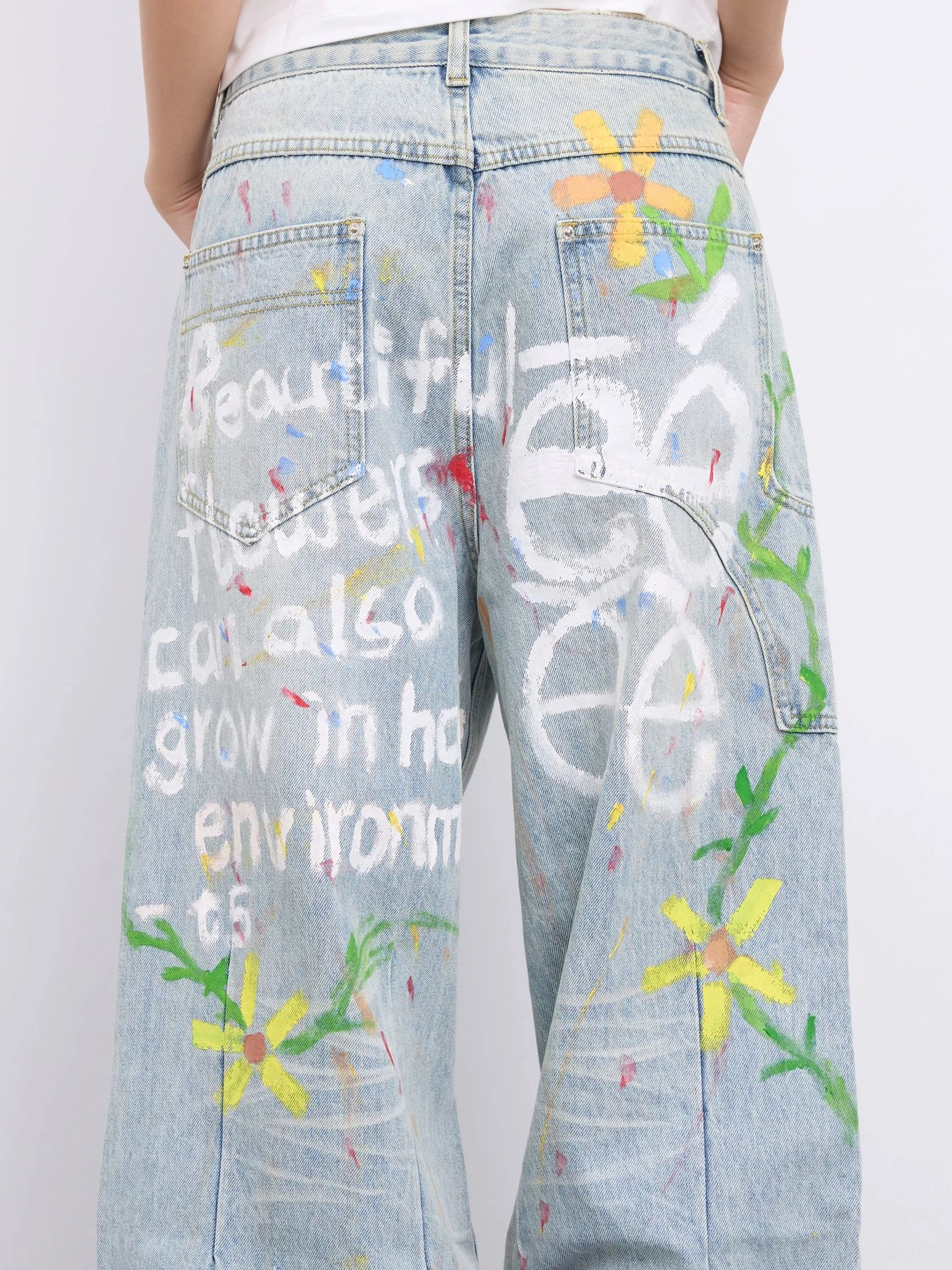 Back view of washed blue doodle jeans featuring hand-painted phrases floral vines paint splatters and classic denim pockets