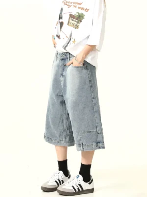Front side view of washed blue wide-leg denim culotte shorts with button fly, side pockets, stitched hem, graphic white T-shirt, and retro sneakers