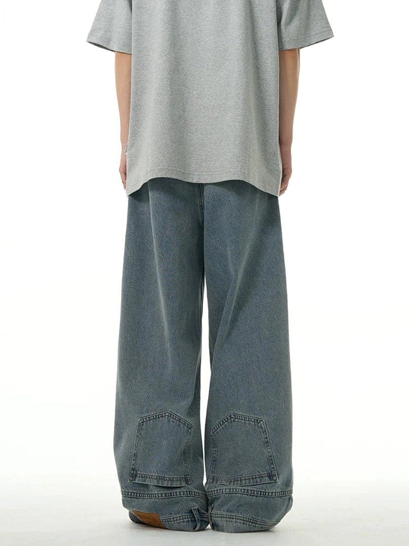 Back view of washed blue women’s wide-leg jeans with lower-leg utility patch pockets, layered denim cuffs, and relaxed avant-garde streetwear shape