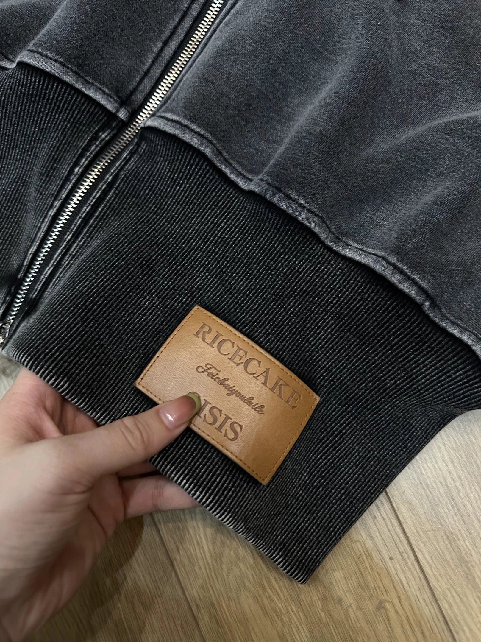 Close-up of the ribbed cropped hem on a vintage washed hoodie with textured fleece fabric and a brown leather-look decorative patch