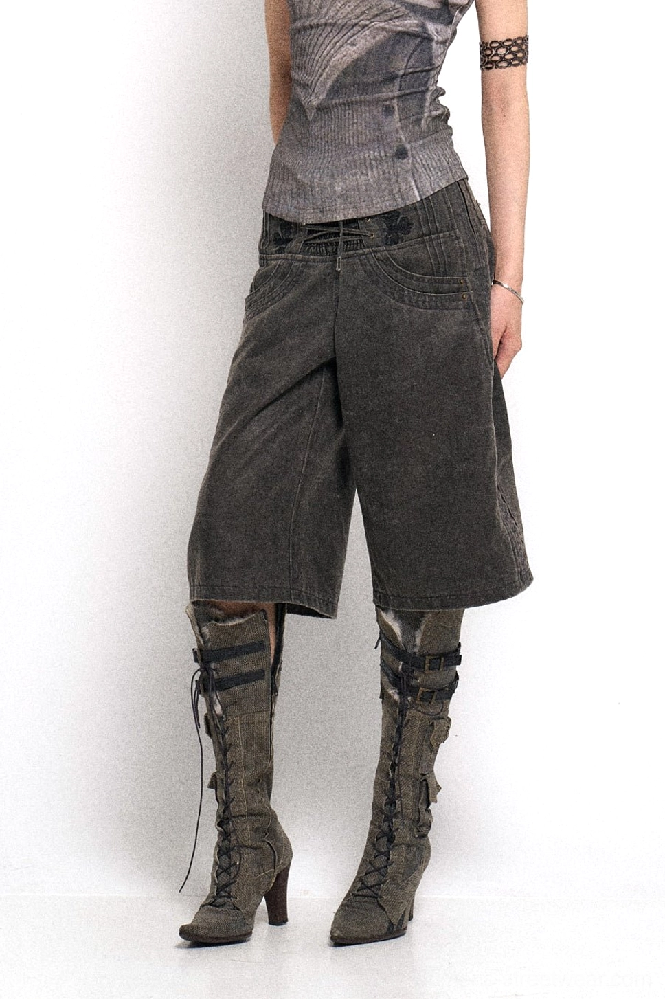 Dark grey washed wide-leg denim culotte pants with high-rise lace-up corset waist, oversized front pockets, and distressed streetwear texture shown in a low-angle studio view