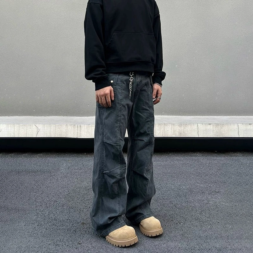 Model wearing washed gray utility cargo pants with oversized black hoodie, sunglasses, tan work boots, and wide-leg streetwear styling