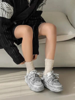 Female model wearing washed grey wavy platform sneakers with cream ribbed socks and a black knit outfit in a relaxed indoor setting