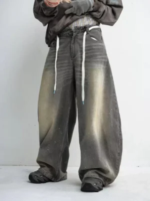 Washed grey wide leg drawstring jeans shown from a low front angle with sun-faded denim, paint speckles, oversized legs, and adjustable streetwear waist