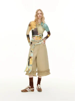 Full-body front view of washed khaki ruffle hem culottes with a printed long sleeve top, scarf waist belt, and retro sneakers