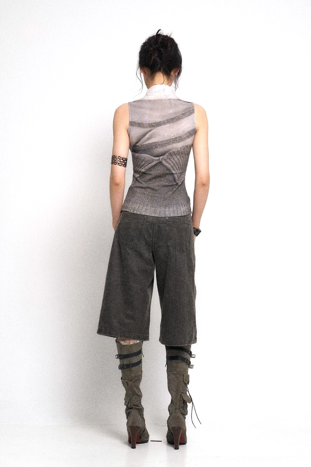Back view of washed dark grey wide-leg denim culotte streetwear pants styled with a printed top and lace-up heeled boots against a studio background