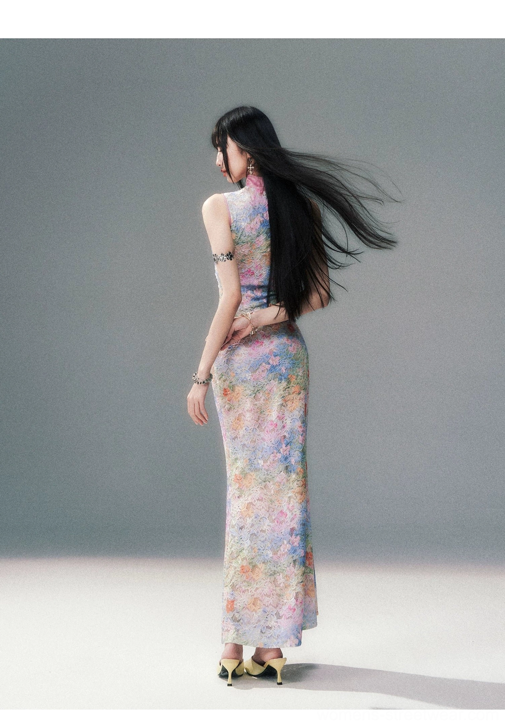Back view of a woman wearing a fitted floor length watercolor floral cheongsam maxi dress with a sculpted back silhouette, pastel botanical print, high heels, and flowing hair