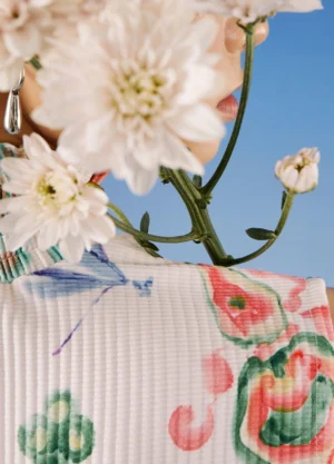 Close-up view of white ribbed qipao dress fabric with watercolor floral artwork and delicate dragonfly print details