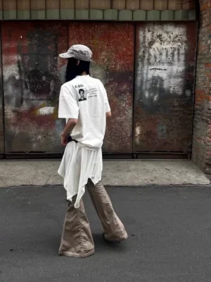 White oversized Whatever Guitarist graphic tee shown from the back with subtle E BOI punk print in an urban alley