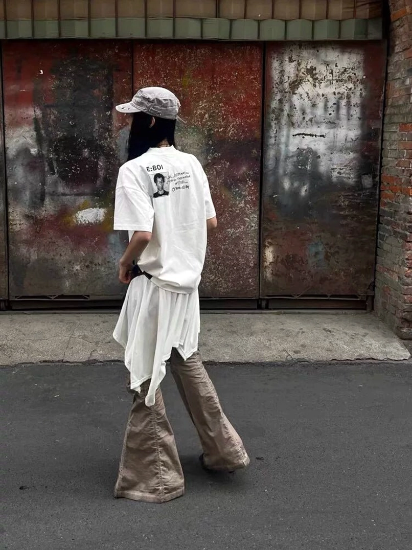 White oversized Whatever Guitarist graphic tee shown from the back with subtle E BOI punk print in an urban alley