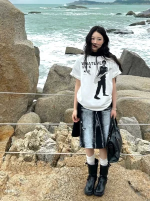 White Whatever Guitarist oversized graphic tee with black guitarist print and bold punk lettering worn on a rocky beach