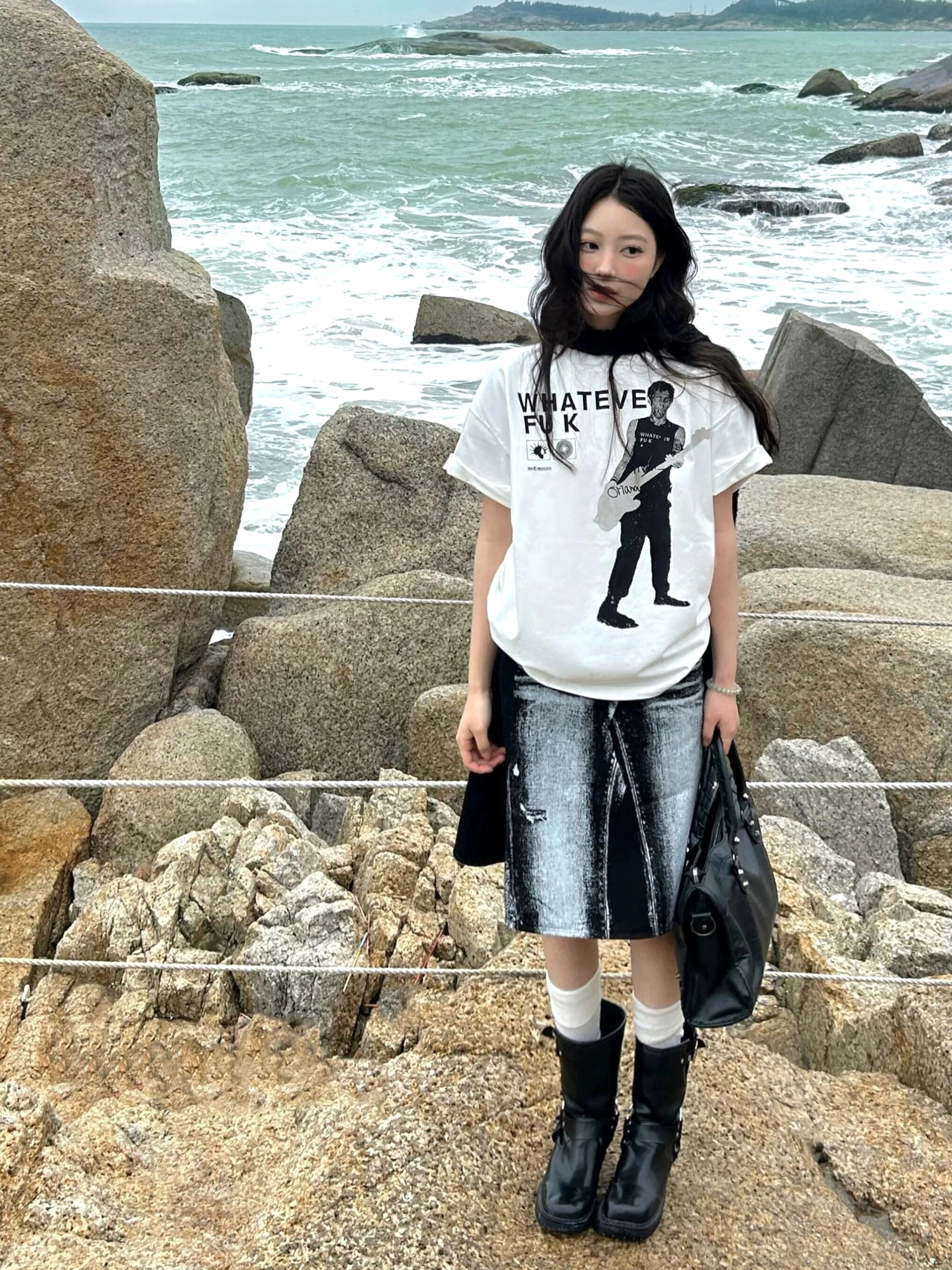 White Whatever Guitarist oversized graphic tee with black guitarist print and bold punk lettering worn on a rocky beach