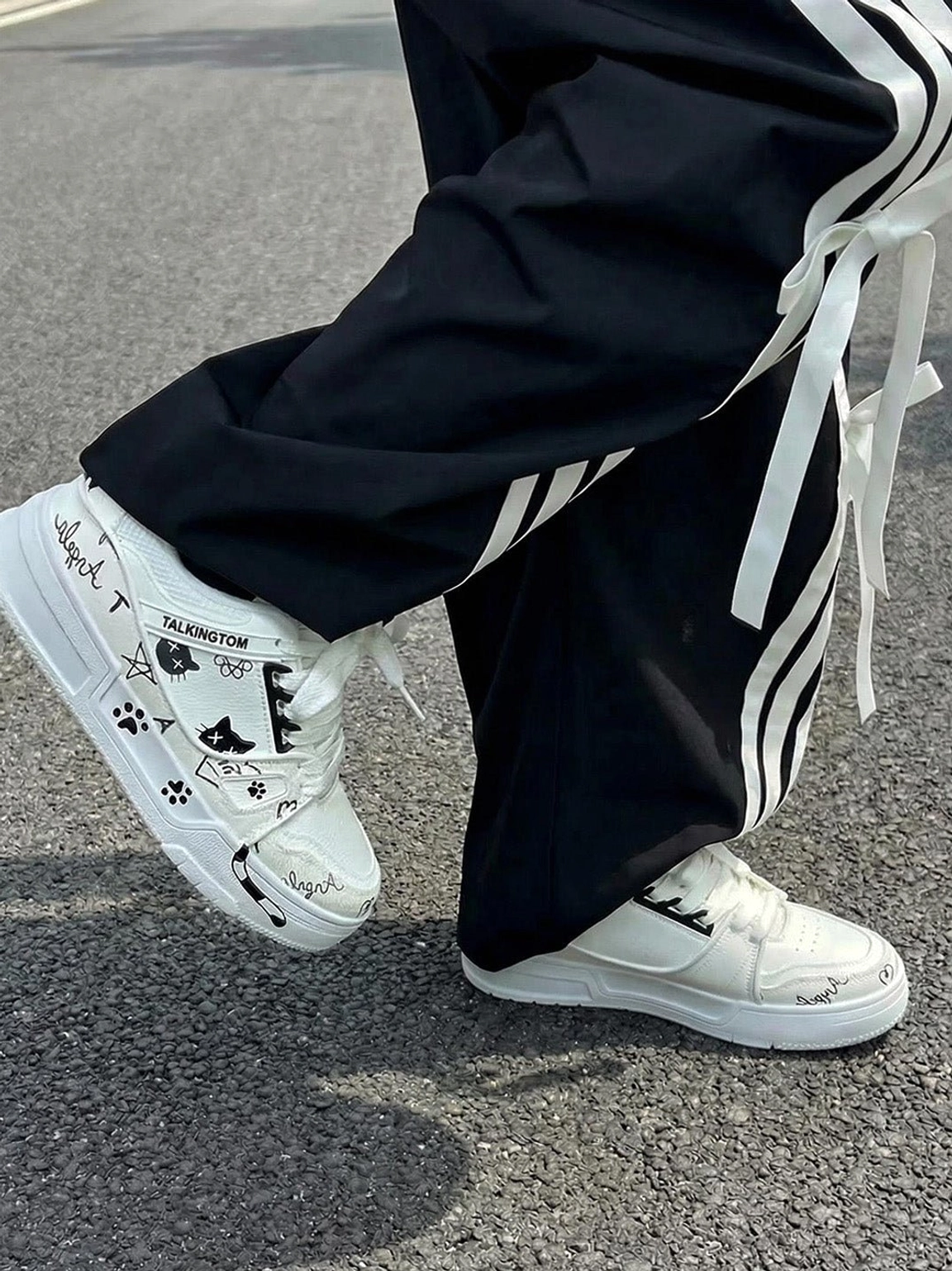 White anime cat print low-top sneaker worn with black striped track pants in a casual urban streetwear look