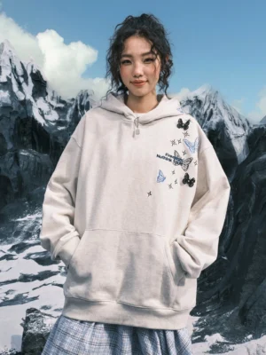 Front view of a White Ash oversized streetwear hoodie with butterfly and star embroidery worn outdoors in a snowy mountain setting