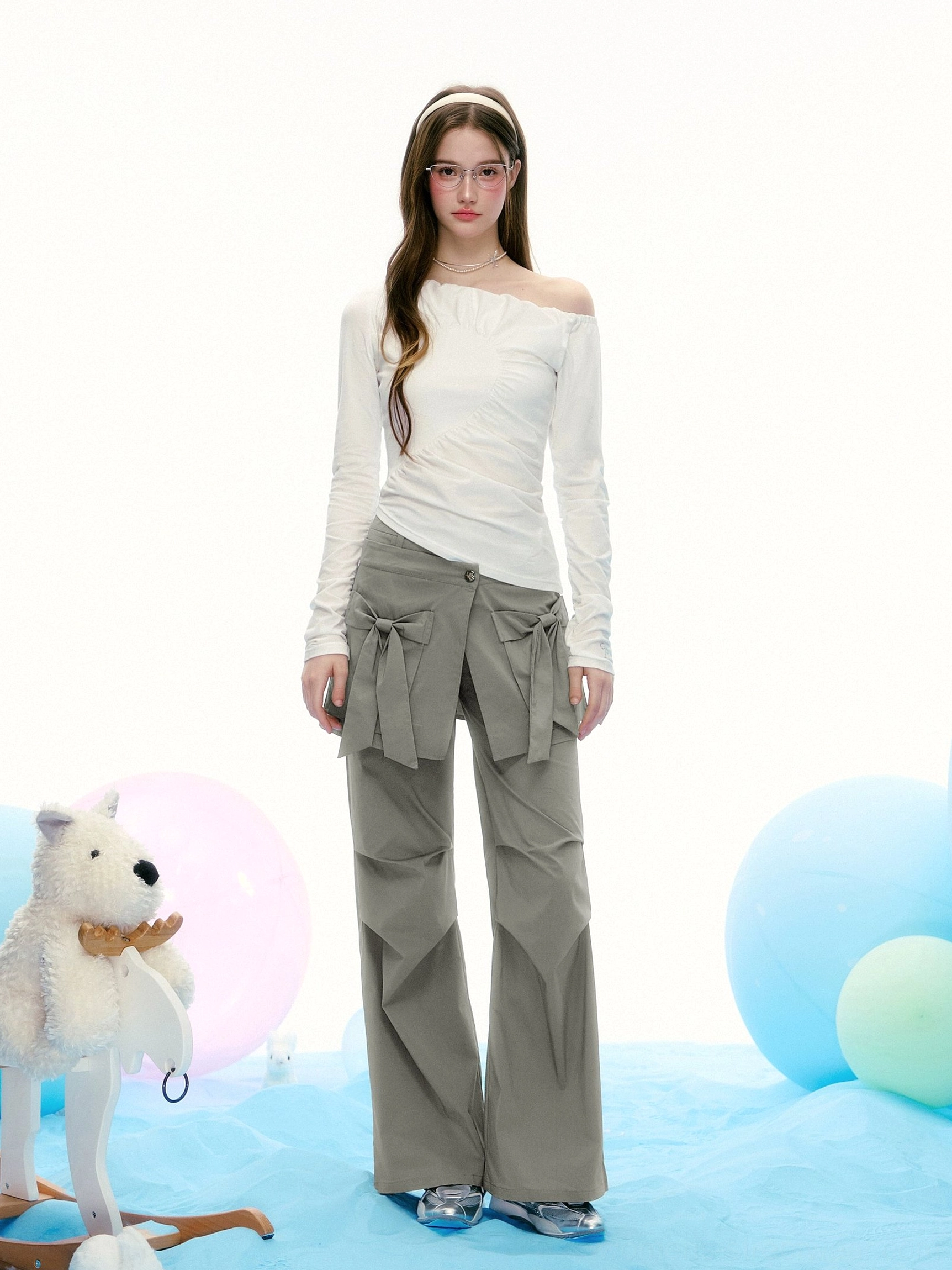 Full-body front view of a white asymmetrical long sleeve top with diagonal ruching styled with grey bow decorated wide-leg trousers in Seoul-inspired fashion