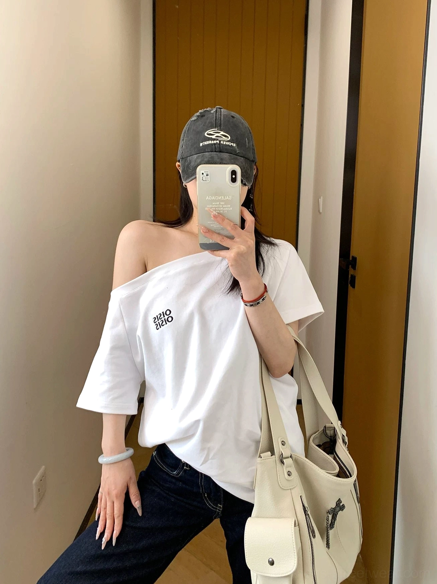 Front view of a white loose off-shoulder logo T-shirt styled with dark jeans and a beige tote bag
