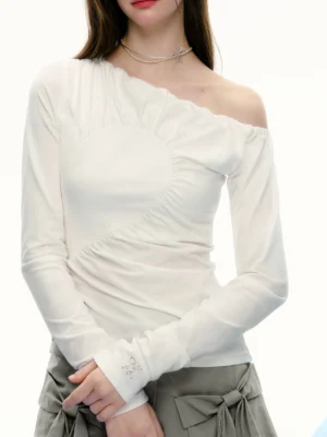 Close-up front view of a white asymmetrical off-shoulder long sleeve streetwear top with diagonal ruched seam, exposed shoulder, slim fit, and subtle cuff embroidery