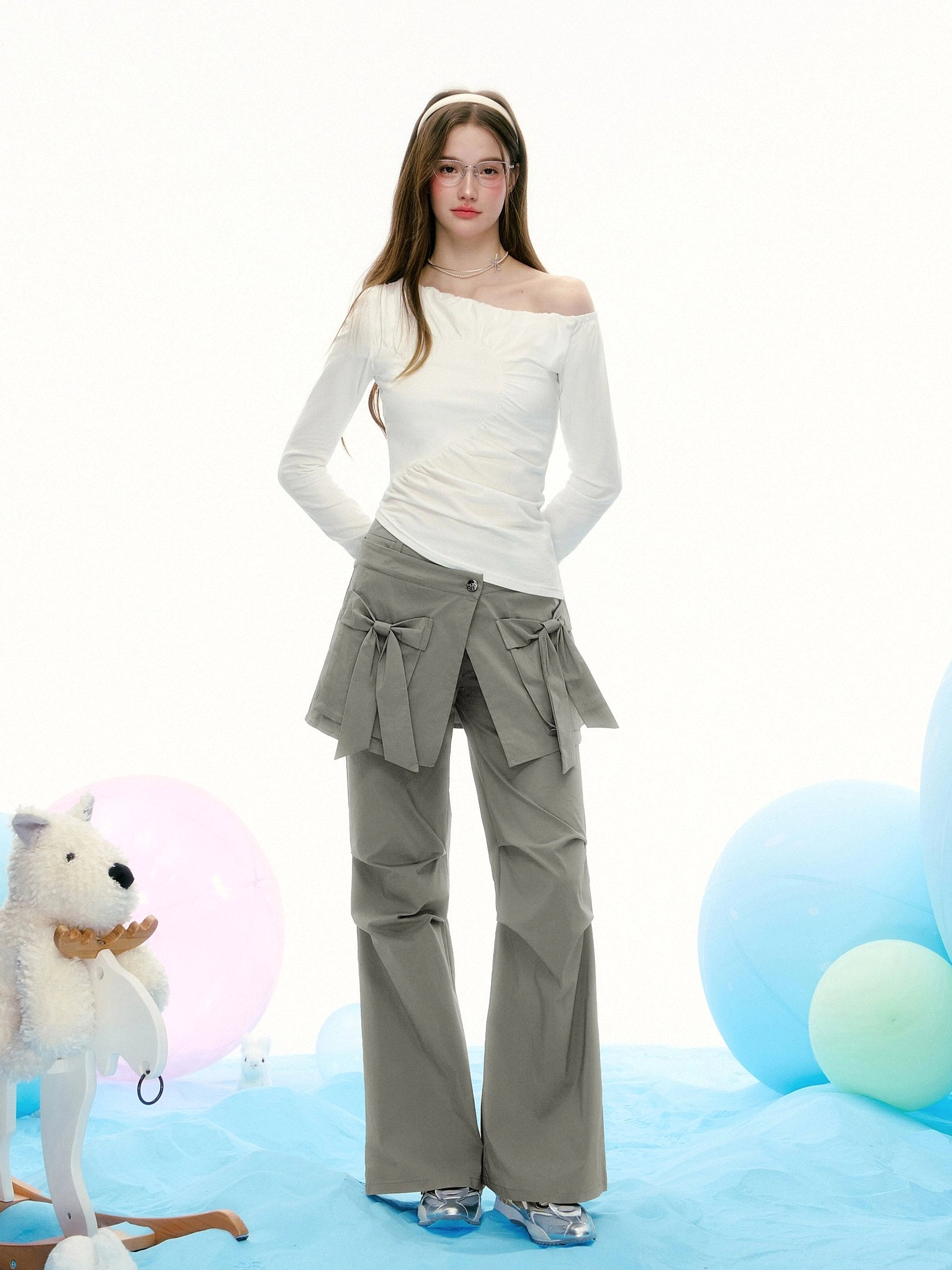 Full-body styling view of a white asymmetrical off-shoulder streetwear top paired with grey wide-leg bow detail pants in a contemporary Korean fashion outfit