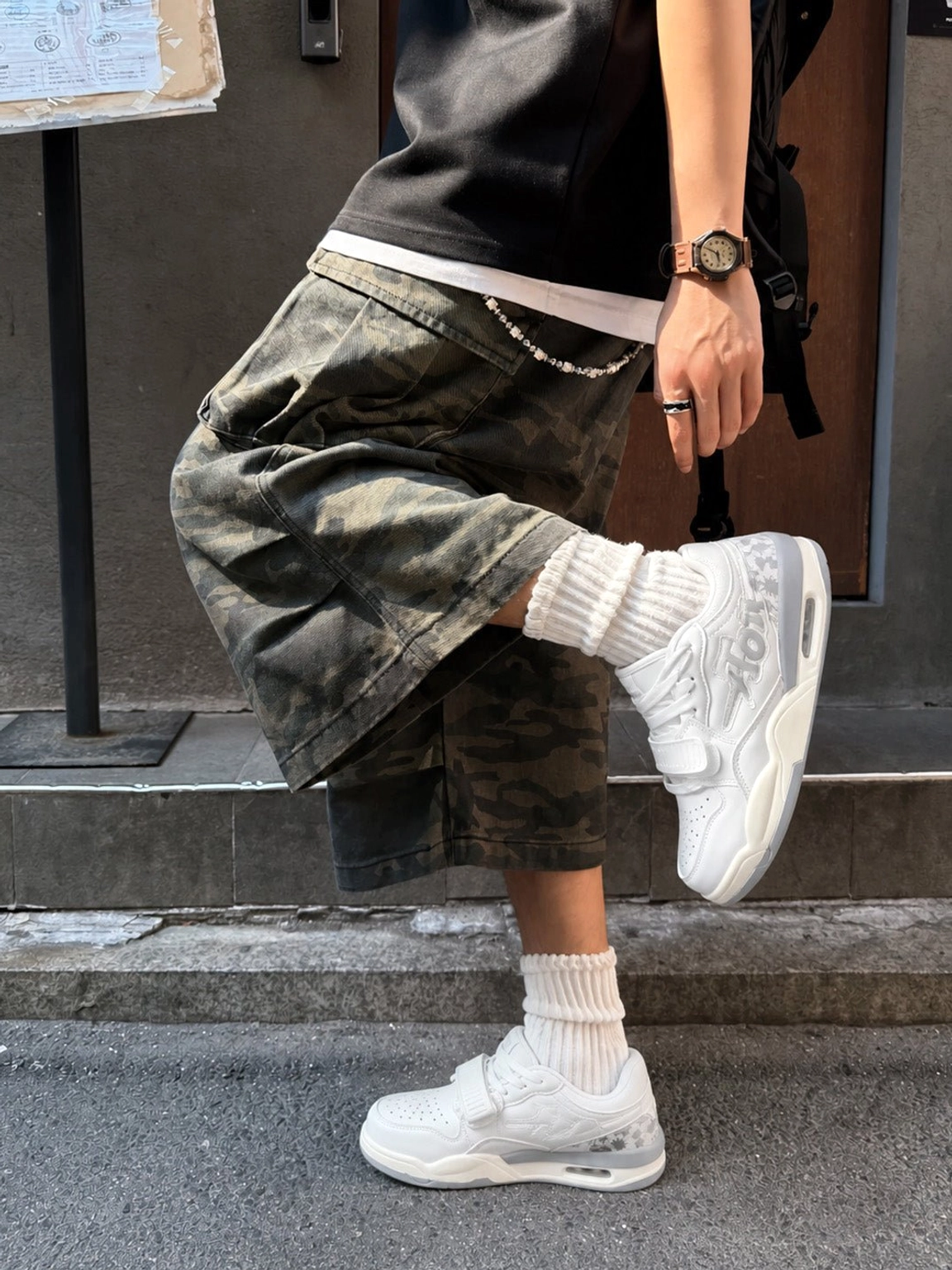 White basketball-inspired court sneakers styled with camouflage cargo shorts, white crew socks, and a contemporary urban streetwear outfit
