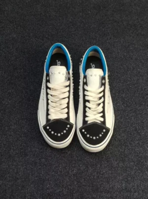 Top-down view of paired white pearl-studded skate sneakers with black suede-style toe caps, clean white laces, and bright blue inner lining