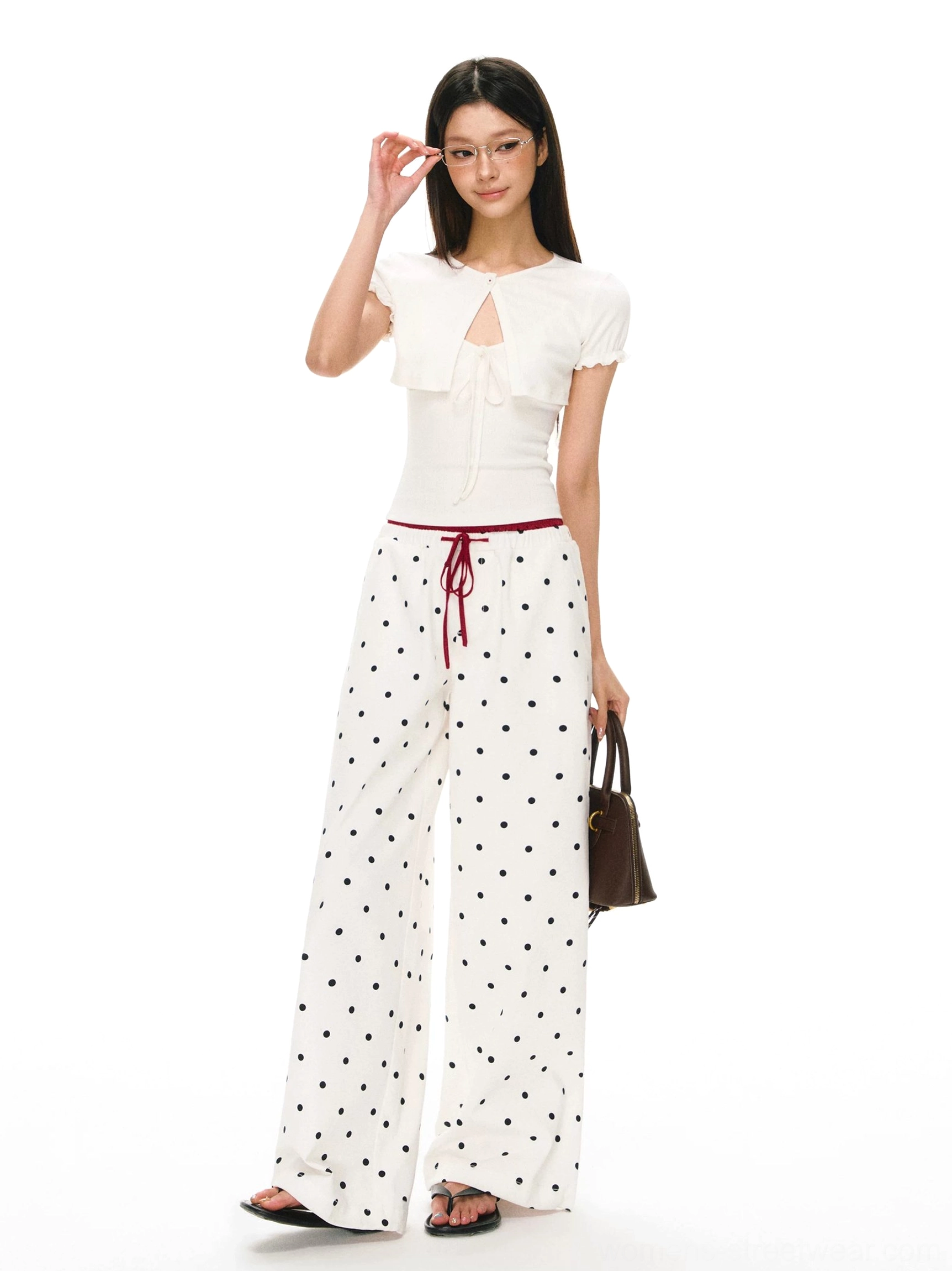 Full front view of white and black polka dot wide leg pants styled with a cropped top and brown handbag for a Y2K streetwear outfit
