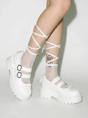 Model wearing white double buckle platform Mary Jane shoes with lace-up fishnet socks in an alternative streetwear outfit