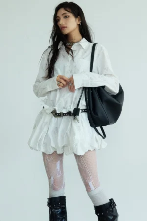White bubble hem mini shirtdress styled with a waist belt patterned fishnet tights buckle knee boots and black tote bag