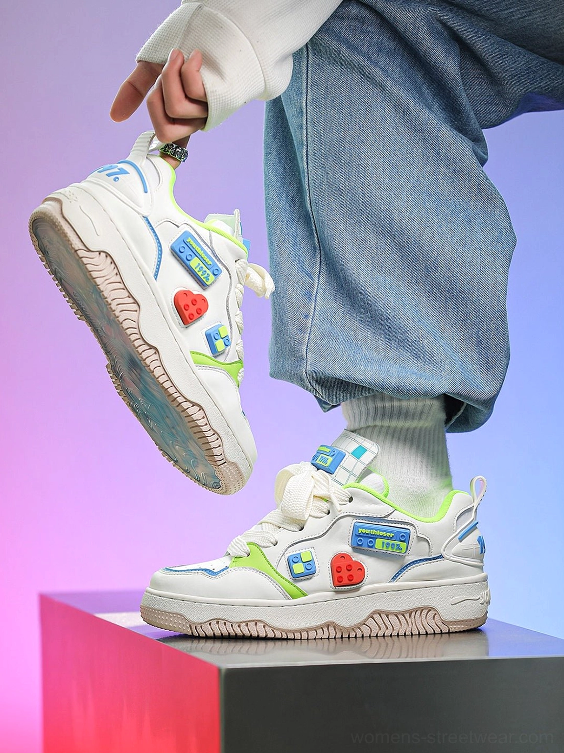 Low-angle view of white building block chunky skate sneakers held against a purple pink background showing colorful side patches and textured platform outsole