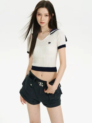 Full front view of a cream white cable knit cropped sailor collar top with navy blue trim, embroidered chest detail, and fitted short-sleeve silhouette styled with navy cargo shorts