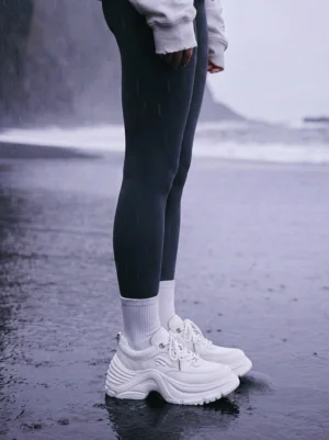 White chunky dad sneakers styled with dark leggings and white crew socks in a low rear coastal fashion view