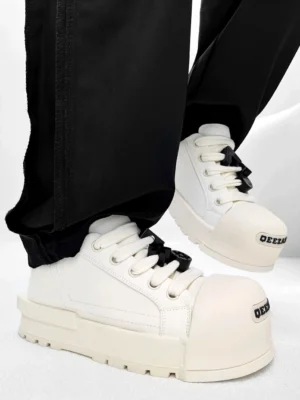 White chunky platform sneakers with black laces and decorative lace charms worn with black straight leg trousers