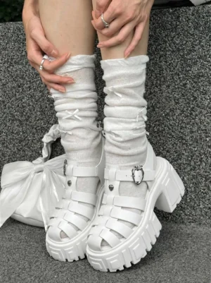 White chunky platform Roman sandals styled with slouchy ruffle socks and a white bow handbag on dark stone steps