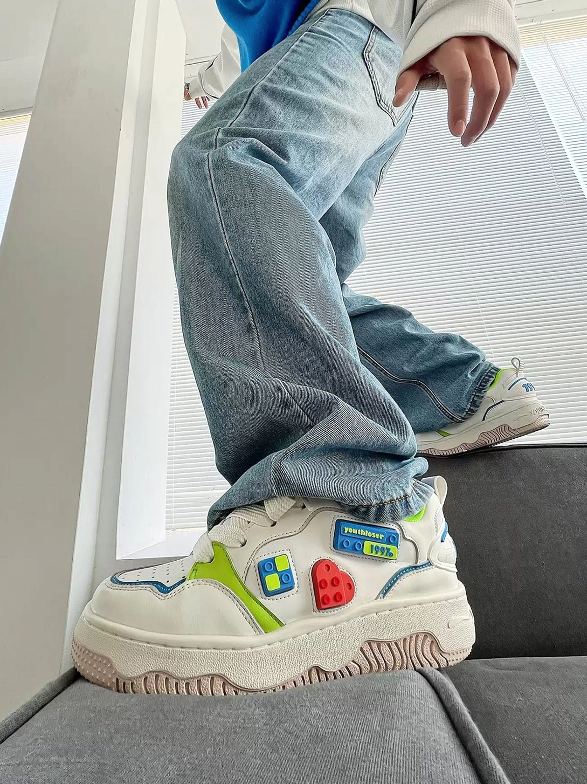 Model wearing white chunky platform skate sneakers with colorful building block details styled with baggy light blue jeans in a casual streetwear outfit