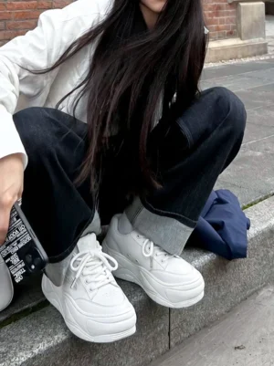 Woman wearing white chunky platform sneakers with a casual minimalist streetwear outfit in an urban setting