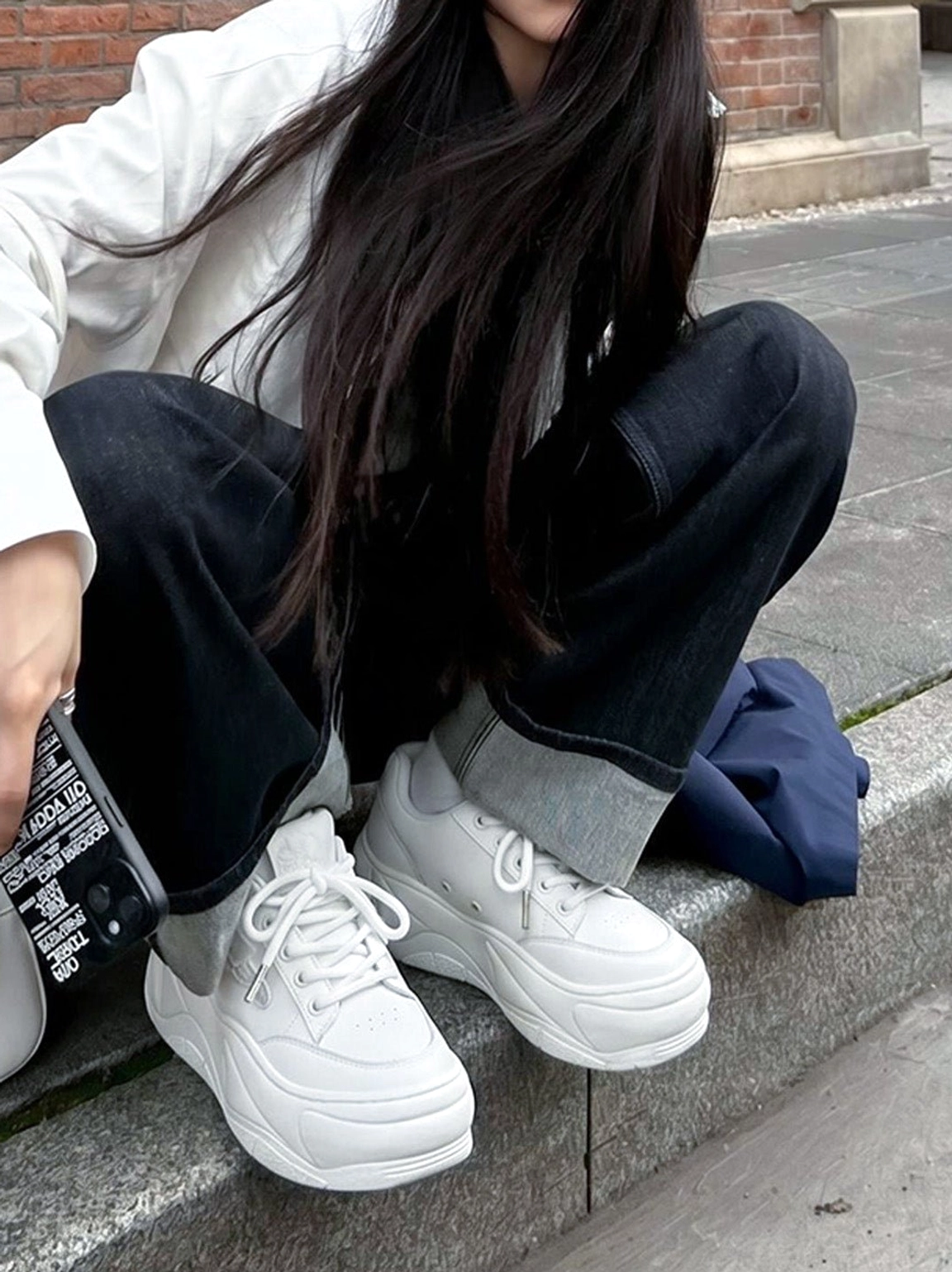Woman wearing white chunky platform sneakers with a casual minimalist streetwear outfit in an urban setting