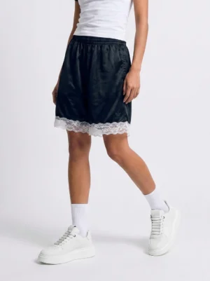 Female model wearing white chunky platform sneakers with white socks, a white tank top, and black lace-trimmed shorts in a casual streetwear outfit