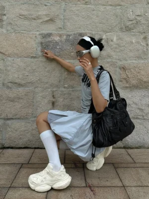 White chunky streetwear sneakers worn with white socks, a blue skirt, gray tee, sunglasses, headphones, and casual urban styling