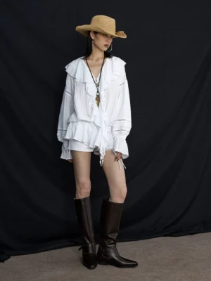 Back three-quarter view of a white cotton ruffled poet blouse with relaxed sleeves, textured stripes, and adjustable hem