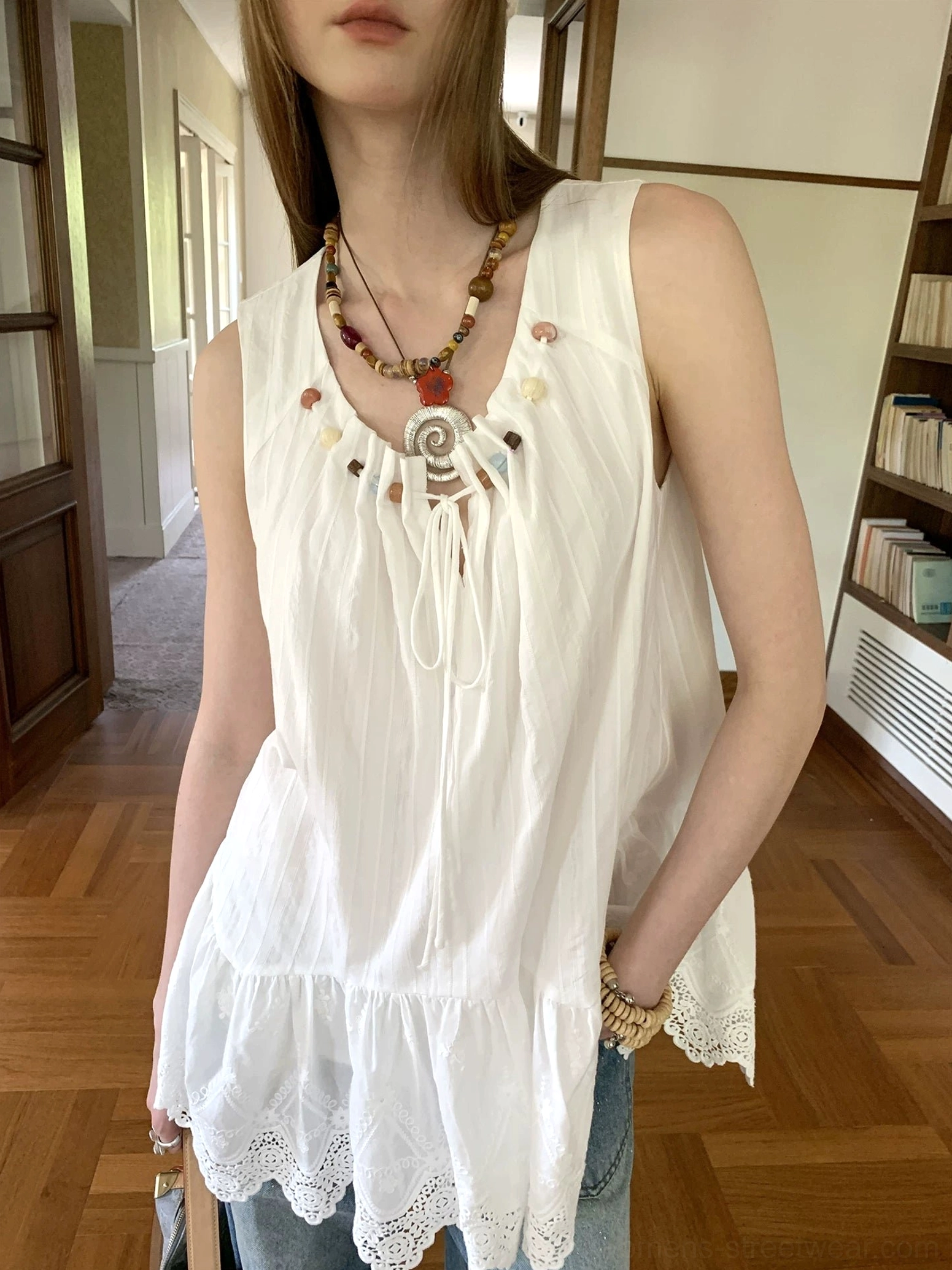 Close-up of white cotton sleeveless tunic top showing textured fabric, decorative beaded neckline ties, and lace hem
