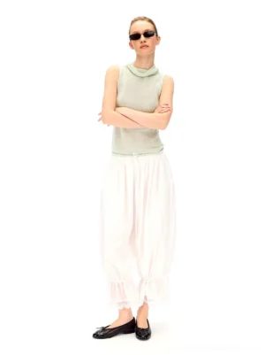 Full outfit view of white cropped balloon streetwear pants styled with a light green sleeveless turtleneck and black sunglasses