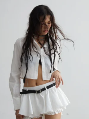 White cropped button-down shirt styled with a low-rise ruffled mini skirt and black waist belt in a Korean streetwear outfit