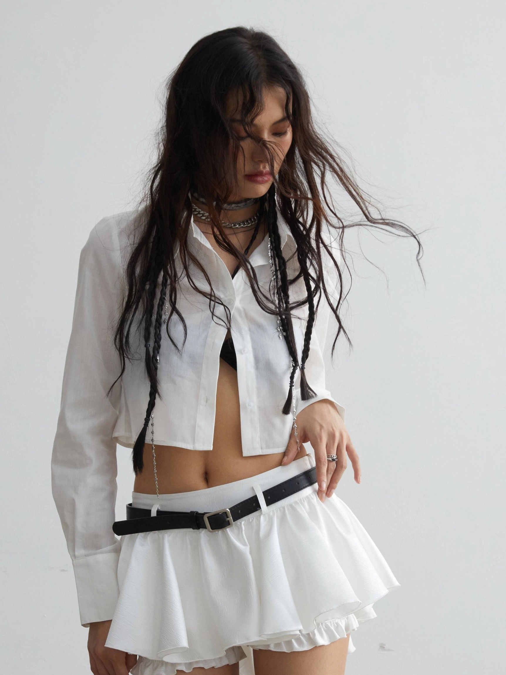 White cropped button-down shirt styled with a low-rise ruffled mini skirt and black waist belt in a Korean streetwear outfit