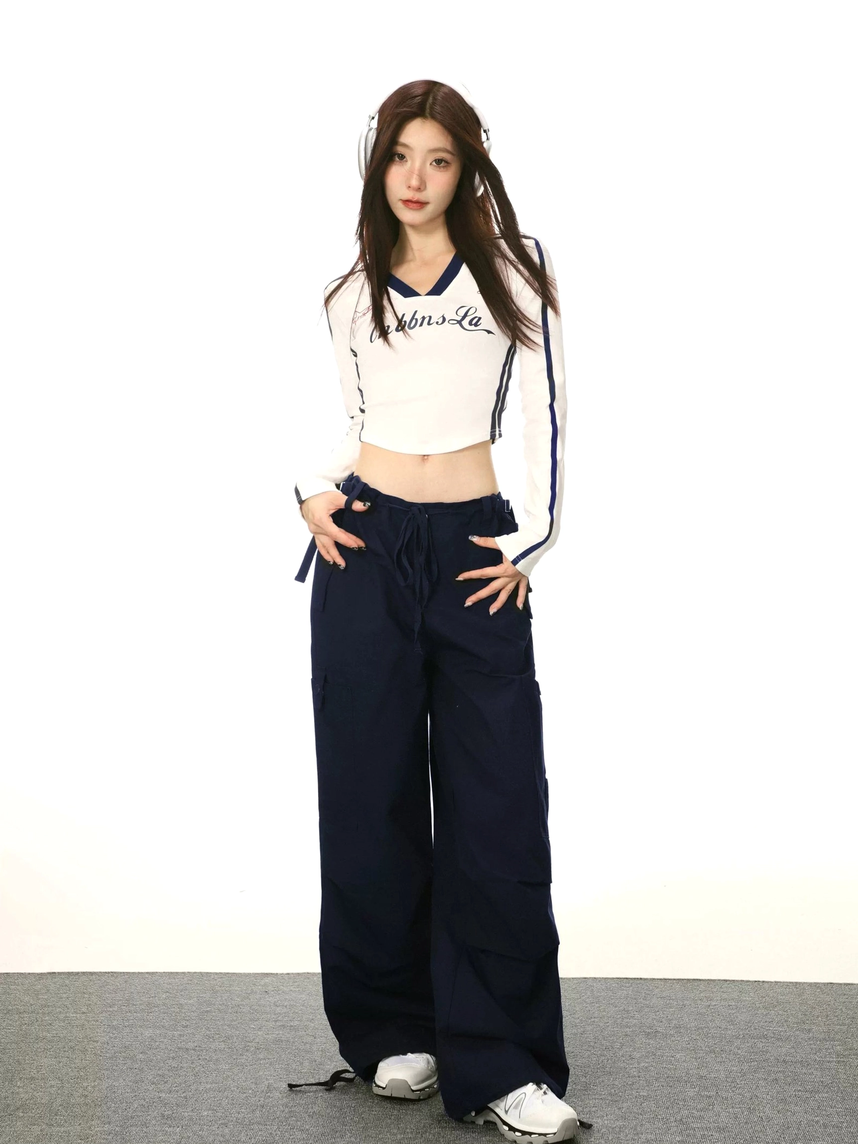 Full-body outfit featuring a white cropped V-neck long sleeve streetwear top with navy stripes, wide-leg cargo pants, and white sneakers