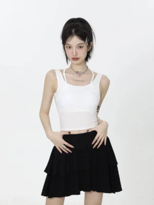 Close-up front view of a white slim fit cropped camisole with double straps styled with a black layered ruffle mini skirt
