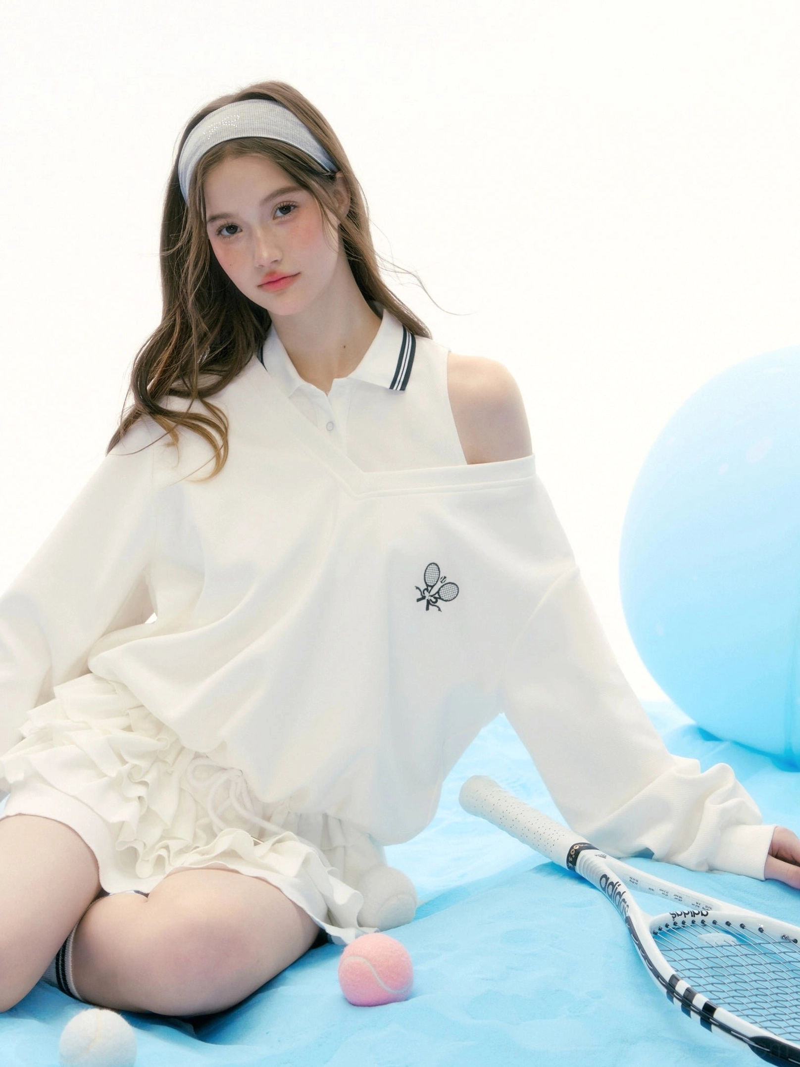 Three quarter view of white cutout shoulder tennis polo and ruffle skirt set with dual racket embroidery