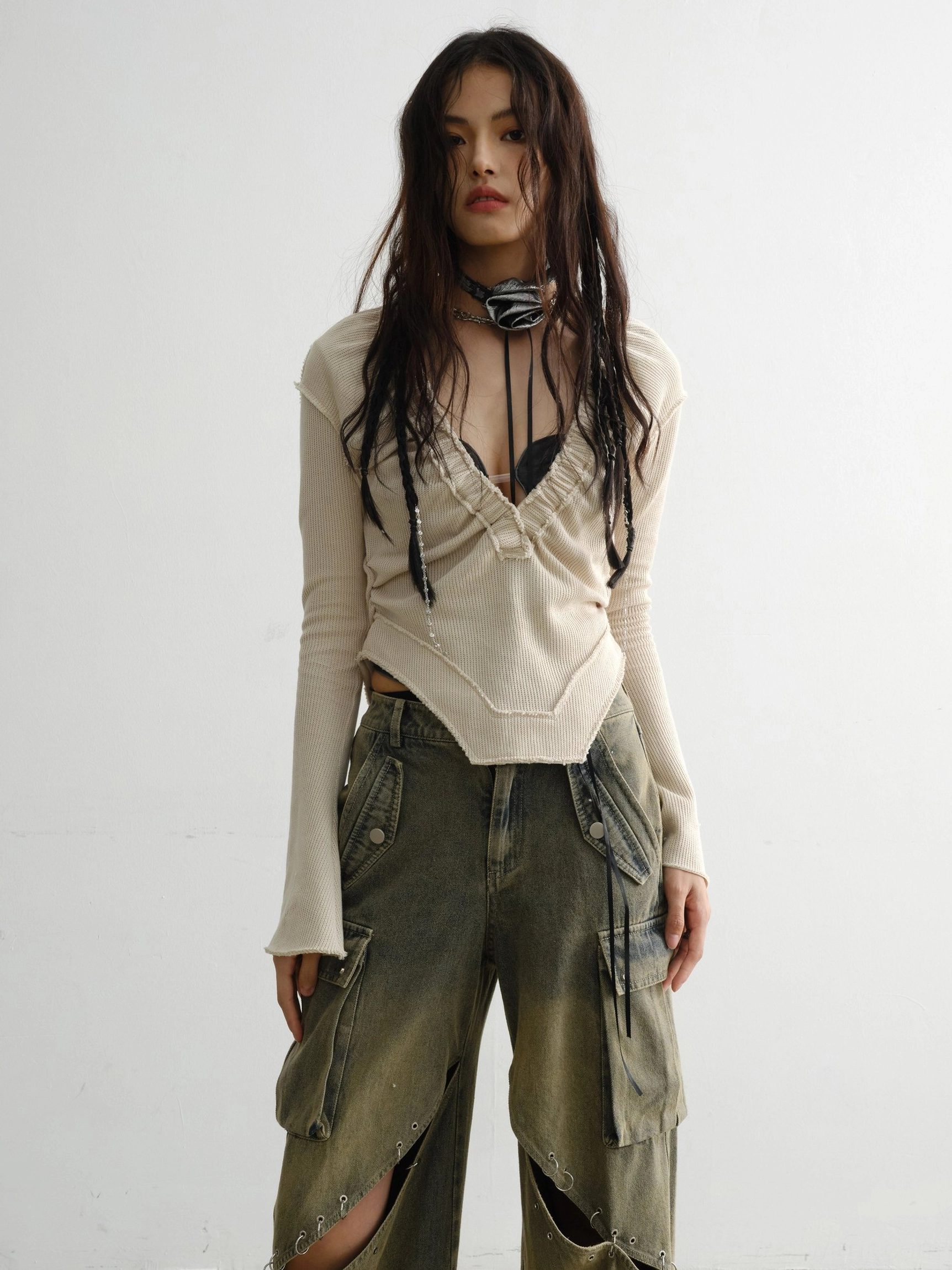 Front view of a white deep V ribbed knit top with ruched neckline, asymmetric hem, flared sleeves, and vintage cargo jeans styling